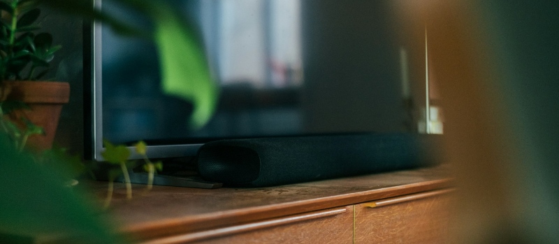 Vad ska du tänka på när du köper en soundbar? Närbild av en TV omgiven av växter ovanpå ett TV-möbel med en soundbar under TV:n.
